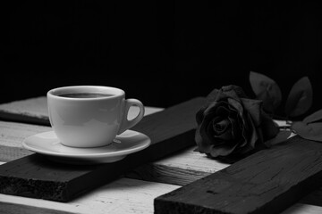 White coffee cup on black boards and black rose on white boards