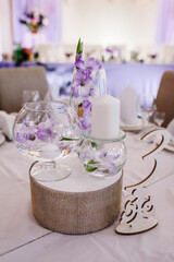 Festive table decorated with composition of violet, purple, pink flowers and greenery, candles in the banquet hall. Table newlyweds in the banquet area on wedding party.