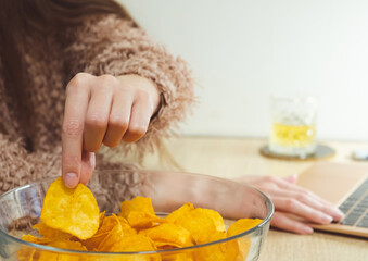 Young woman working at laptop and eating chips