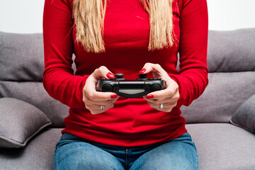 Detail of the hands and the controller of a young woman playing video game at home, dressed in a red sweater. Concept of woman gamer and online game. © Alvaro