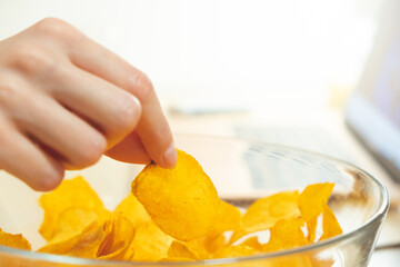 Young woman working at laptop and eating chips