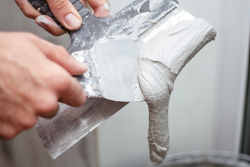 Man's hand removes excess plaster from the spatuia.