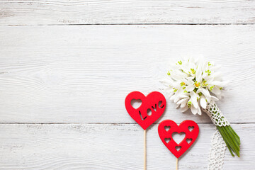 A bouquet of snowdrops and red heart decors on a white wooden background.
