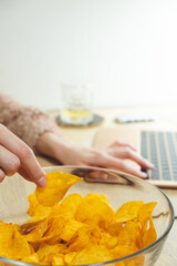 Young woman working at laptop and eating chips
