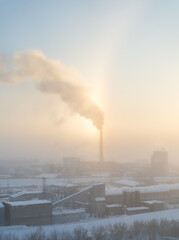 The chimney of a steaming power plant emerges from the back fog. The chimney of the power plant rises above the surrounding fog. Energy. Heating plant in operation.