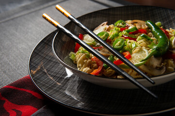 Asian noodles. Noodles with mushrooms and vegetables. Food sticks. Plate with noodles on a dark background.	
