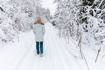 Fototapeta na wymiar Young woman walking on snow covered forest. Beautiful winter time. Back view.