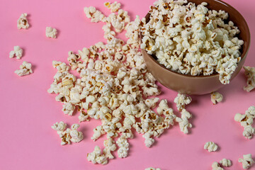 Fototapeta na wymiar Popcorn on a pink background. A full plate of popcorn. Popcorn is scattered around. Movie snack
