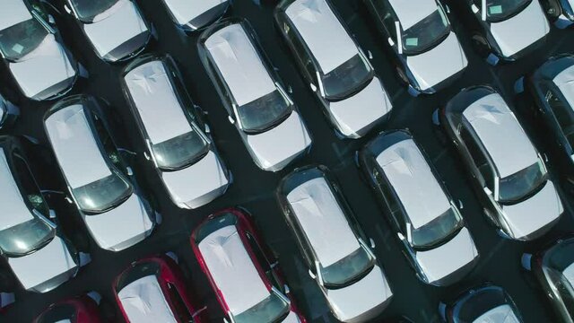 Aerial top down view of new cars parked in car parking lot. Car dealer parking lot full of new automobiles. New cars lined up for import and export business.