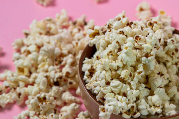 Popcorn on a pink background. A full plate of popcorn. Popcorn is scattered around. Movie snack