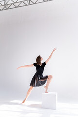 A slender girl in a black sports dress poses while dancing on a white isolated background. Girl athlete dancing on a white isolated background with place for text or logo.