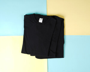 Pile of black folded clothes. Top view of folded black t-shirt isolated with colored background, copy space, flat lay. Blank t-shirt templates are commonly used for mockups and template designs.