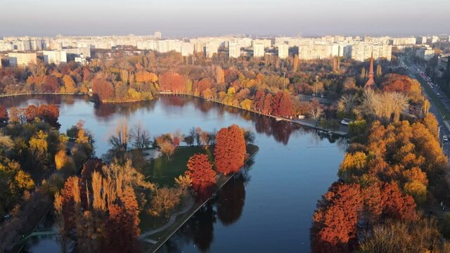 View of the Titan park from the drone with multiple yellowed and red trees, reflecting sky, residential buildings, Bucharest, Romania