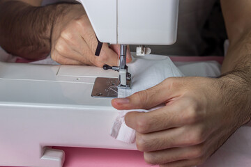 White sewing machine on a pink background. Electric sewing machine. Hands for work on the sewing...