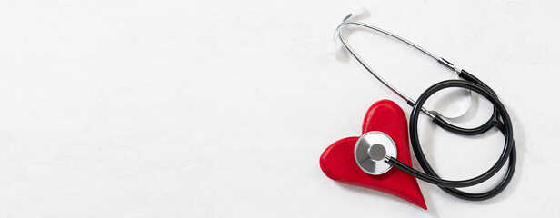 Creative composition with decorative wooden red heart and medical stethoscope on white marble background. World Health Day background. St. Valentine’s day in pandemic concept. Long banner format.