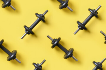 Pattern of black dumbbells on yellow background. Sport and fitness. View from above. Flat lay.