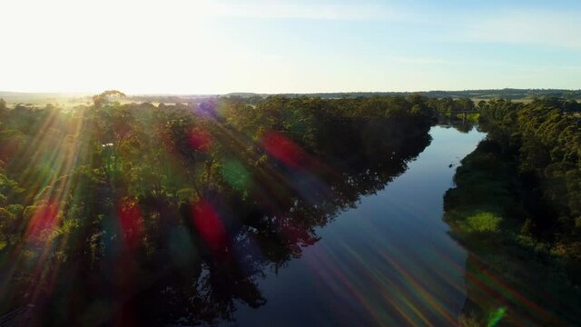 Slow descend over river facing the sun with lens flare at sunset in Australia