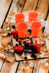set of four liquor fruit alcoholic shot cocktails surrounded by berries and strawberries on a wooden background with ice and lines. cocktail menu bar concept