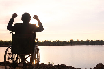 Fototapeta na wymiar Silhouette young disabled man seeing river background.He is raise a hand to and sitting on wheelchair.despair,lonely,hope.Photo concept depression and Patient.