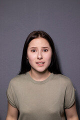 portrait of charming scared brunette woman in marsh color t-shirt on grey wall background. actress acting, emotion