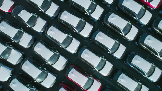 Aerial top down view of new cars parked in car parking lot. Car dealer parking lot full of new automobiles. New cars lined up for import and export business.