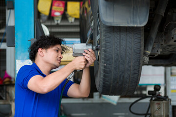 Asian male mechanic worker using pneumatic wrench changing tyre of car at auto repair shop....