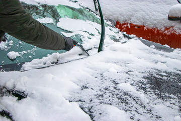 A man is brushing snow from his car. Difficult winter weather conditions for driving a car. Travel fees in a snowy winter