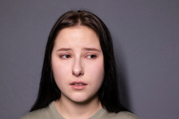 portrait of charming sad brunette woman in marsh color t-shirt on grey wall background. actress acting, emotion