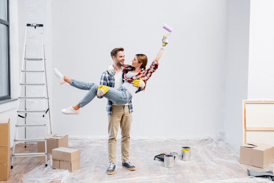 full length of happy young man lifting woman with paint roller at home