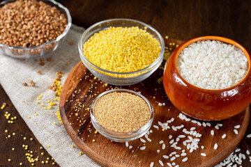 Rice, buckwheat, amaranth and millet in bowls on a brown wooden table. Gluten-free cereals