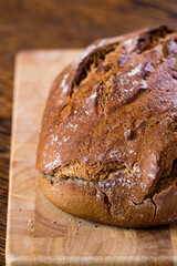 One rustic loaf of freshly baked sourdough bread from a century-old traditional bakery in Berlin. Vertical view of a cropped dark loaf of bread with crusty texture on wooden board