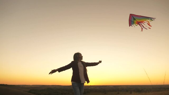 A happy girl runs with a kite in her hands across field in rays of the sunset. The child wants to be pilot. A healthy child dreams of freedom, flight. Kid plays outdoors in the park.