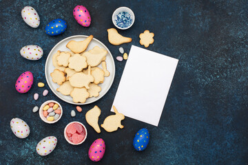 Obraz na płótnie Canvas Festive homemade Easter cookies, chocolate eggs, sugar sprinkling on dark blue wooden background. Happy Easter concept. Copy space, top view.