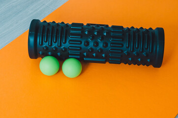 Foam roller and massage balls  on an orange yoga mat at home. Concept: self care practices at home ...