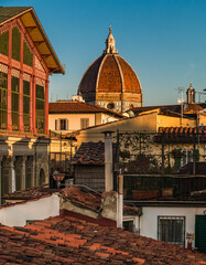Fototapeta na wymiar Lovely view of the dome of Santa Maria del Fiore Cathedral with cupola peeking out of rooftop terraces in the historic centre of Florence at sunset. On the left is the Mercato Centrale building.