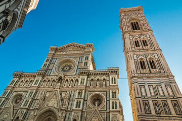 Fototapeta premium Great low-angle view of the beautiful marble facade of the famous Florence Cathedral Santa Maria del Fiore with the free-standing Giotto's Campanile in the Piazza del Duomo on a sunny day with a blue.