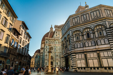 View of Piazza del Duomo in Florence. The square contains the San Zanobi Column next to the Baptistery San Giovanni. Behind is the Santa Maria del Fiore Cathedral with Dome and Giotto's bell tower.