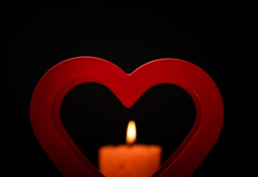Outline of the red heart and soft focus of candlelight on the black background.