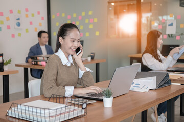 A beautiful woman working on a desk with laptop. She works and smiles happily. She talks on the phone with clients.