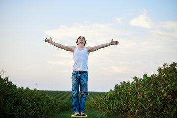 Fototapeta premium Young handsome man, wearing torn jeans and white t-shirt, sitting on yellow stool on green field, thinking. Artistic education concept. Creative portrait outside.