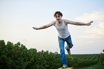 Fototapeta premium Young handsome man, wearing torn jeans and white t-shirt, sitting on yellow stool on green field, thinking. Artistic education concept. Creative portrait outside.
