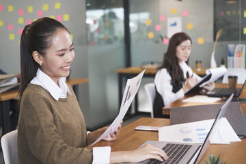 Businesswoman typing on laptop holding papers preparing report analyzing work results in office.