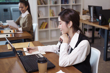 A beautiful office worker sitting in front of a computer in the office of the company. Asian woman sitting at work smiling happily..business managers working with new startup.
