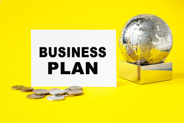 Text BUSINESS PLAN . Globe and wooden cubes on a YELLOW background. The concept of world business, marketing, finance.