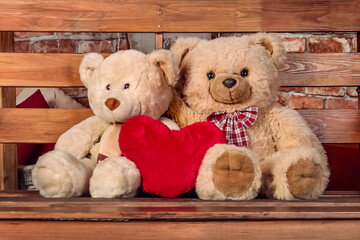 two teddy bears are sitting on a bench next to a soft toy heart