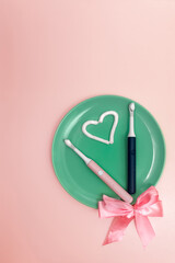 composition with a heart made of toothpaste and two electric toothbrushes on the background of a green dish with a bow