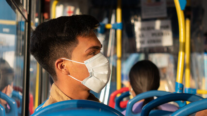 Latino passenger using public transportation to go to study, while wearing a white surgical mask to prevent viral diseases