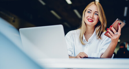 Positive female freelancer working on laptop and smartphone