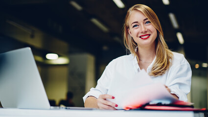 Smiling lady working remotely in cafe with laptop and papers