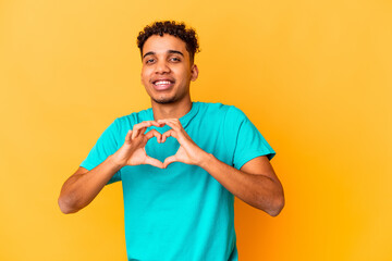 Young african american curly man isolated on purple smiling and showing a heart shape with hands.